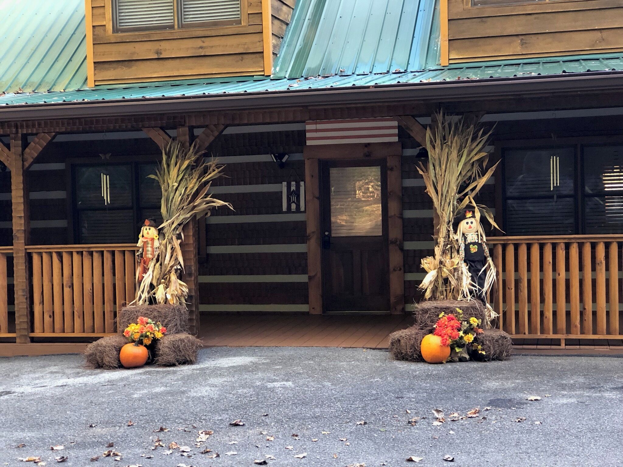 A wooden building with a porch, two decorative scarecrows with pumpkins, and a door with a window above it.