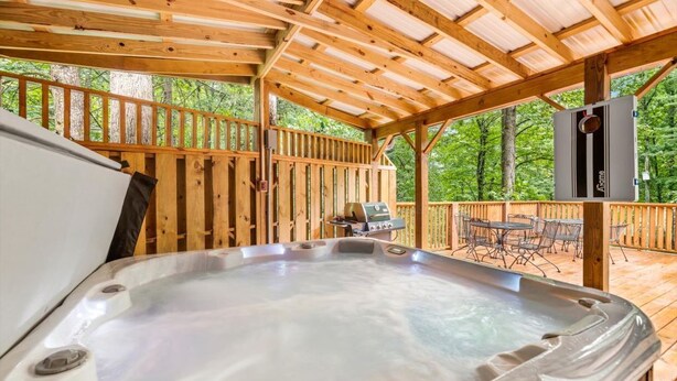 En træterrasse med jacuzzi, udendørs møbler og grillområde.