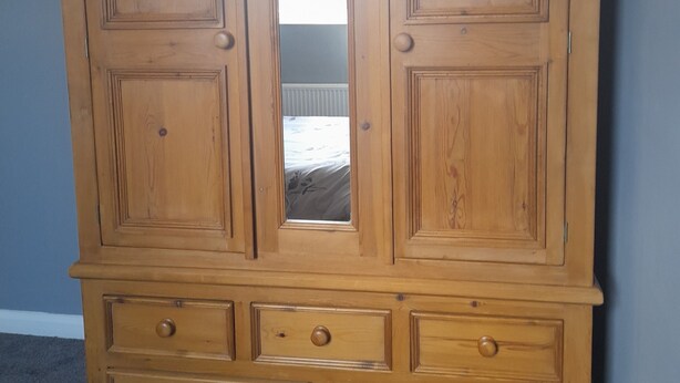 Ein hölzerner Kleiderschrank mit zwei Türen und einem Spiegel, ausgestattet mit mehreren Schubladen und einer kleinen Ablagefläche.