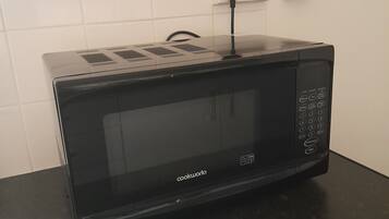 A black Cookware microwave on a dark countertop with a power outlet in the background.