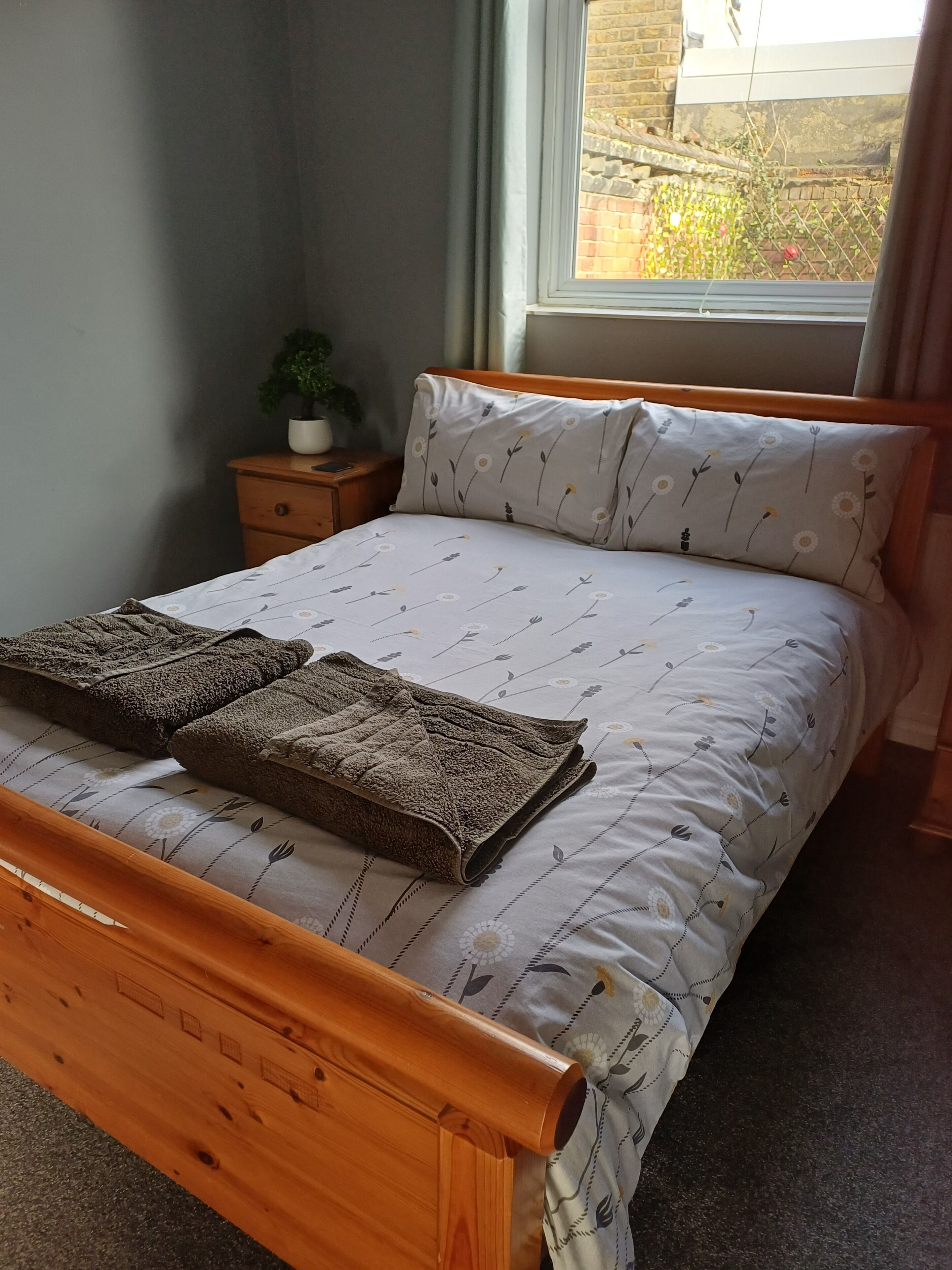 Un lit bien fait, recouvert d’une couvre-lit à motifs floraux, avec deux serviettes pliées posées dessus.