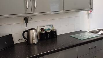 Una cocina con armarios grises, encimera negra y un hervidor. Hay tres recipientes etiquetados como té, café y azúcar.