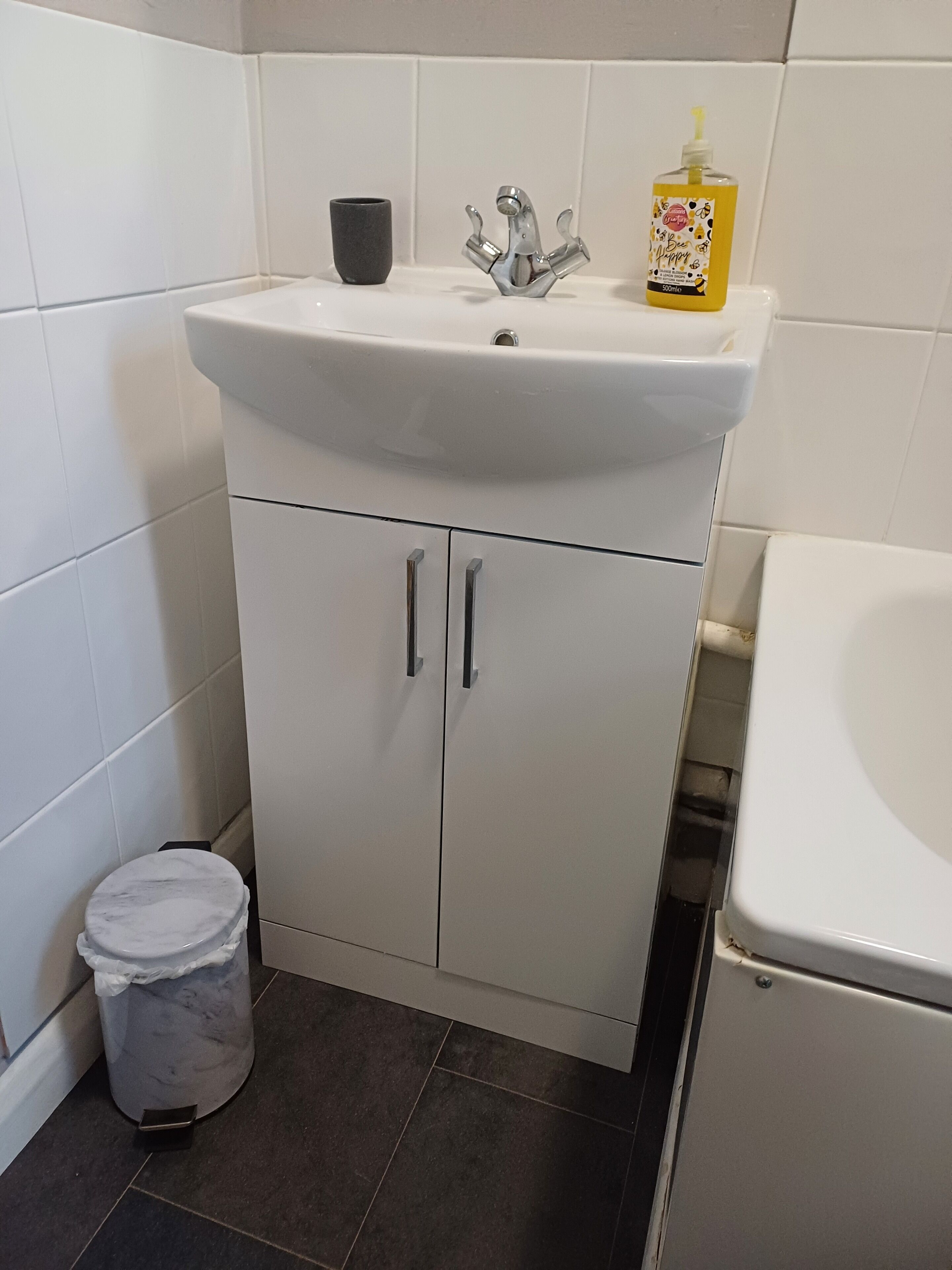 Une salle de bain avec un lavabo blanc, des toilettes et une poubelle.