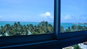 Blick aus einem Fenster auf einen tropischen Strand mit Palmen und dem Meer.