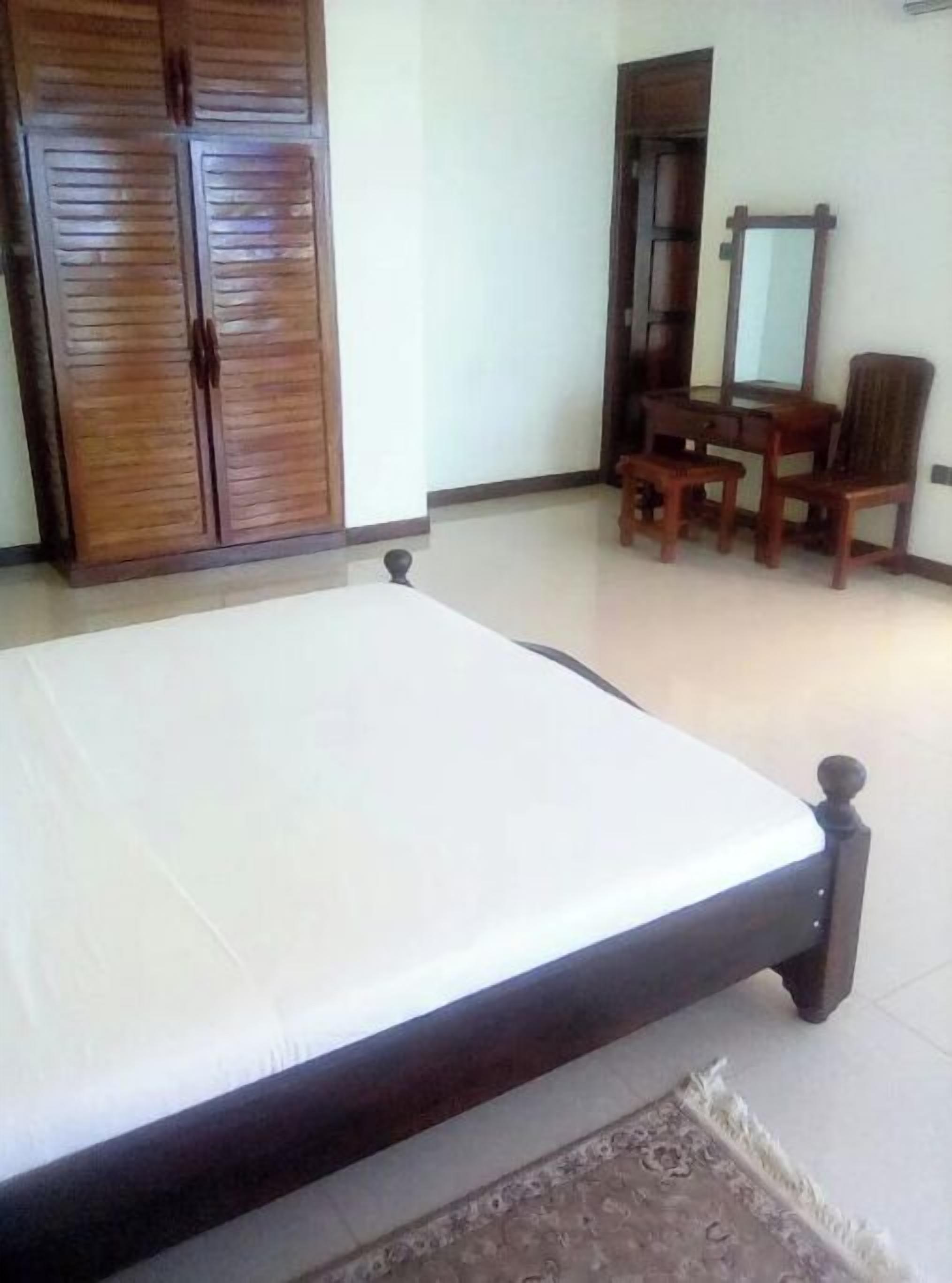 A bedroom with a bed, wooden wardrobe, and a desk with a chair.