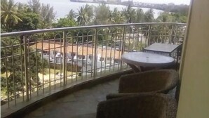 Ein Balkon mit Tisch und Stühlen, einem Metallgeländer und Blick auf ein Gewässer sowie Palmen.