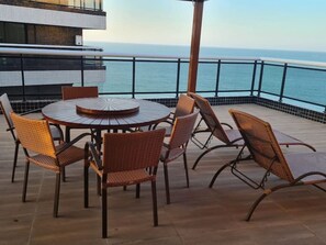 Une table ronde entourée de chaises en osier, sur un balcon offrant une vue sur la mer.