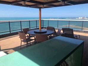 Un espace extérieur abrité, aménagé avec des sièges, et offrant une vue sur la plage et l’océan.