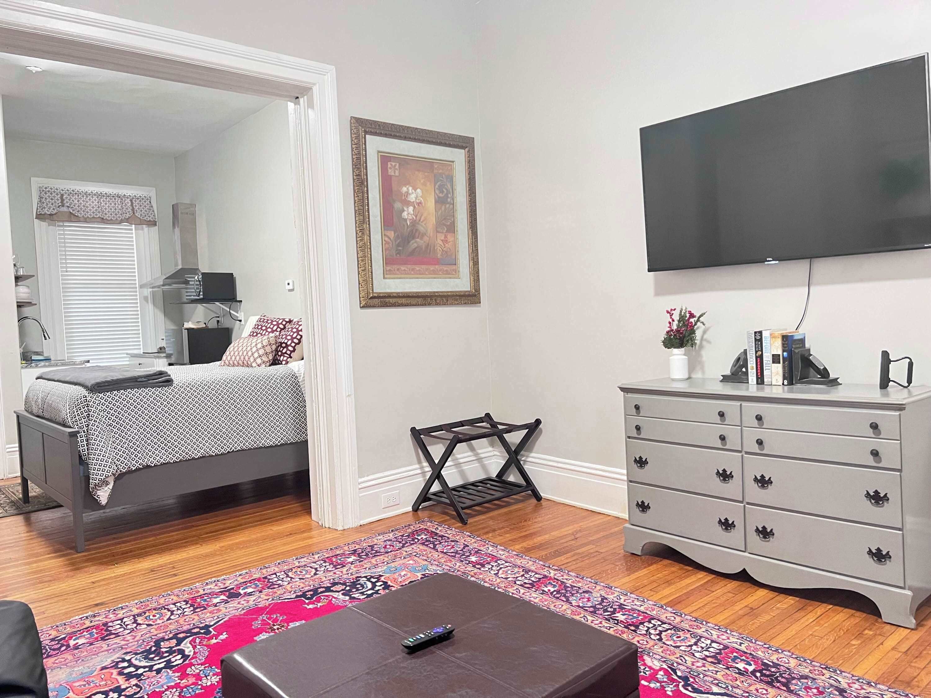 A bedroom with a bed, a dresser, a TV, and a patterned rug.
