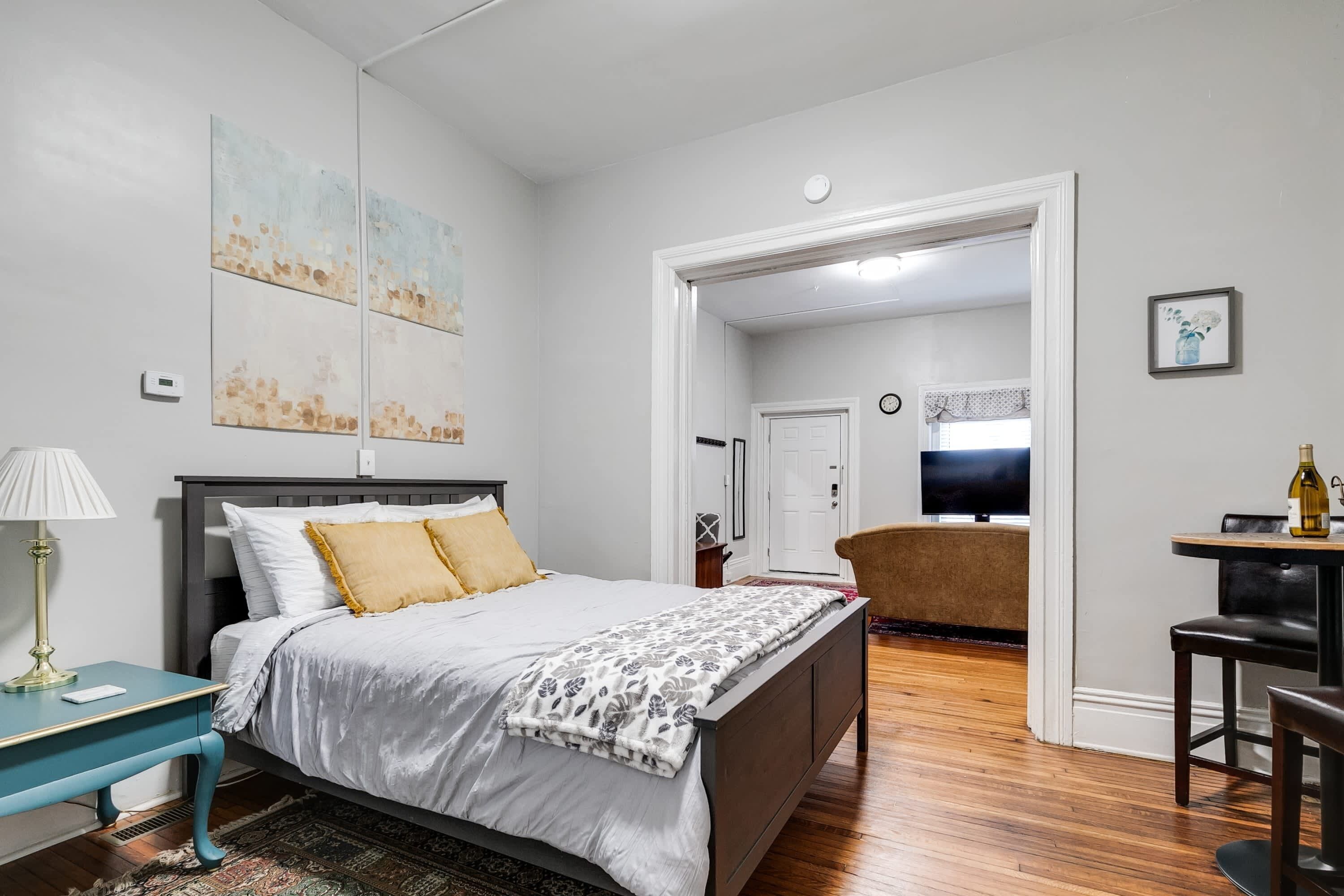 A bedroom with a bed, bedside table, and a chair. There is a door leading to another room.