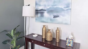 Ein Zimmer mit einer dunklen Holztruhe, einer weißen Lampe, dekorativen Vasen, einem Gemälde eines Sees und einer Topfpflanze.