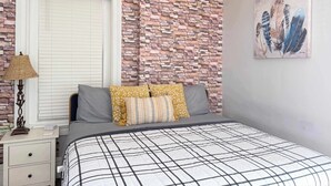 Ein Schlafzimmer mit einer Ziegelwand, einem Bett mit kariertem Überwurf und einem Bild an der Wand.