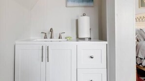 A white bathroom vanity with a sink, two faucets, and a toilet paper holder.