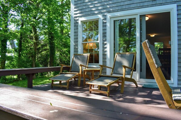 A wooden deck with four wicker chairs and a bench, overlooking a lush green landscape.