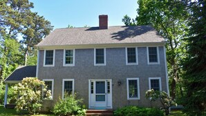 A two-story house with a front porch, a chimney, and a well-maintained lawn. - Four bedroom home within walking distance to Bayside Brewster beaches! (Brewster)