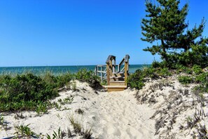 A wooden beach structure with a staircase leading to a platform, surrounded by sand and vegetation.