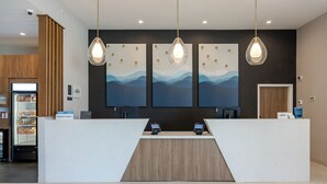 A reception desk with a white counter and wooden accents, two receptionists' stations, and three wall-mounted artwork depicting abstract landscapes.