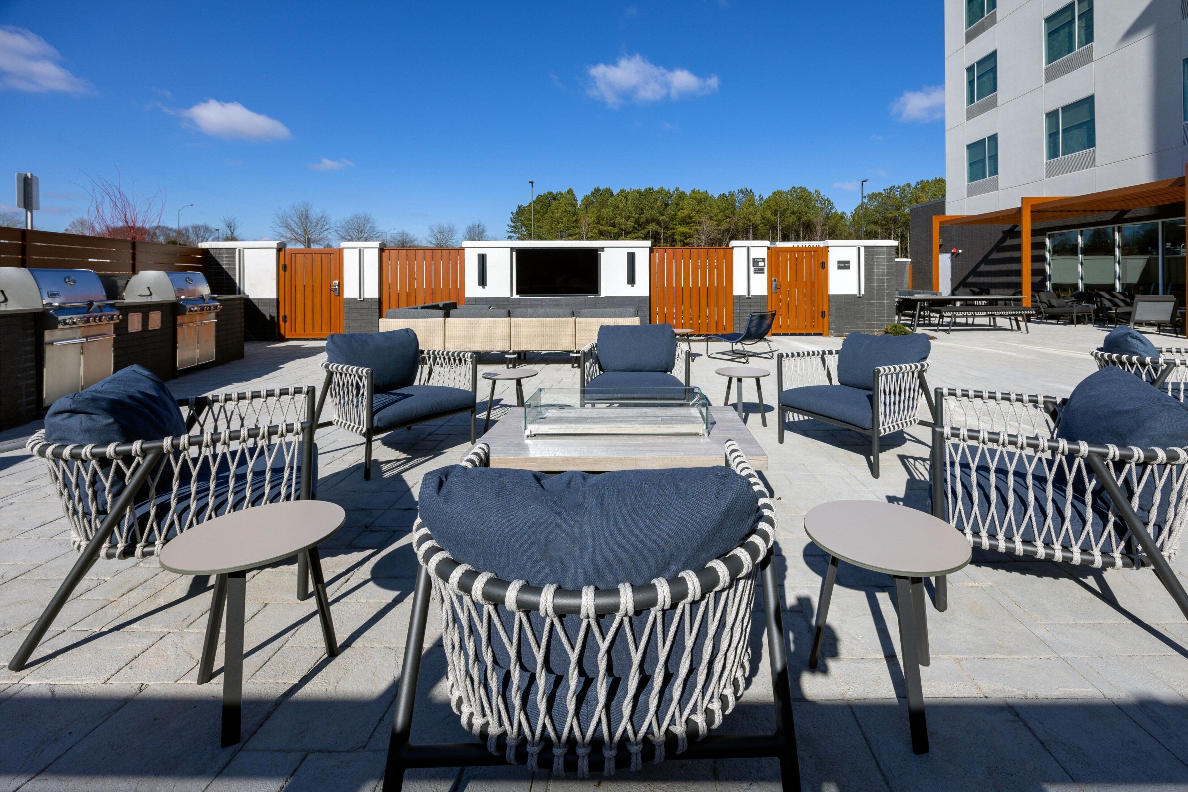 An outdoor seating area with wicker chairs and tables, a barbecue grill, and a building in the background.