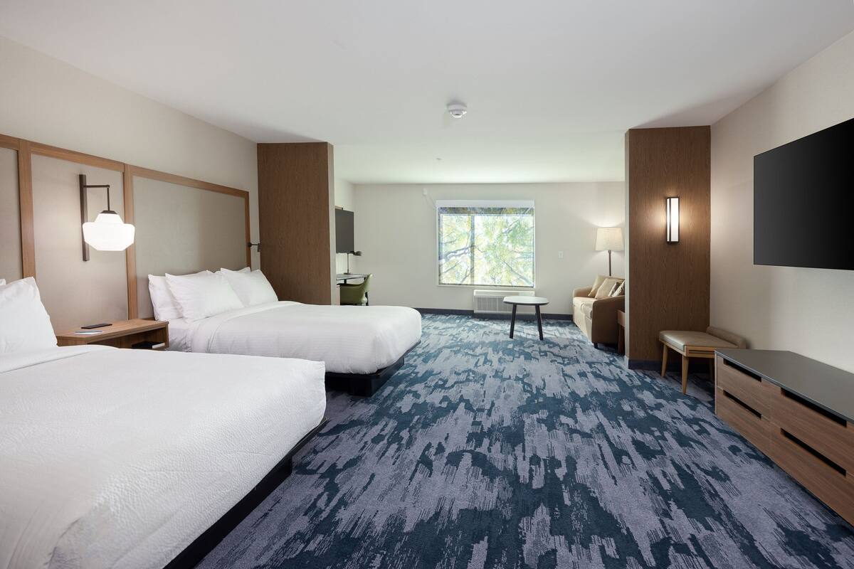 Habitación de hotel con dos camas, un escritorio, una silla, un televisor y una ventana con vista a árboles.