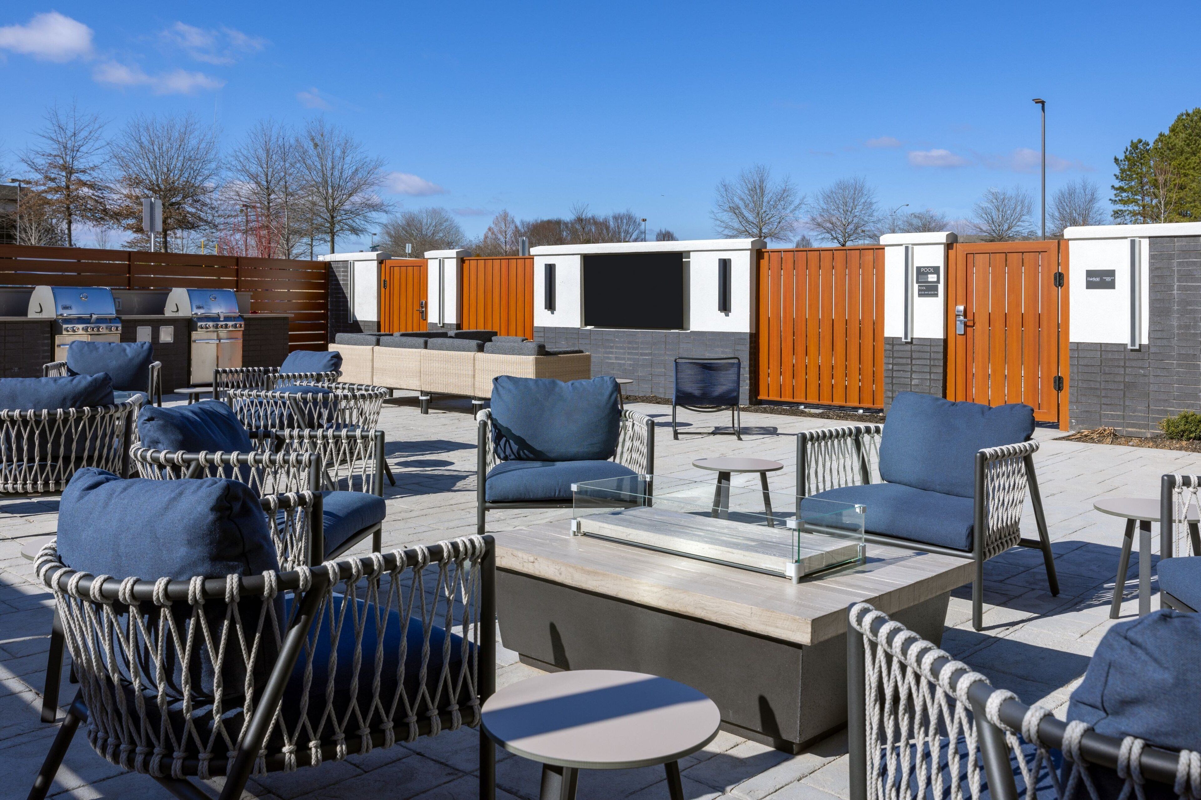 An outdoor patio area with wicker furniture, a fire pit, and a view of a building with a wooden fence.