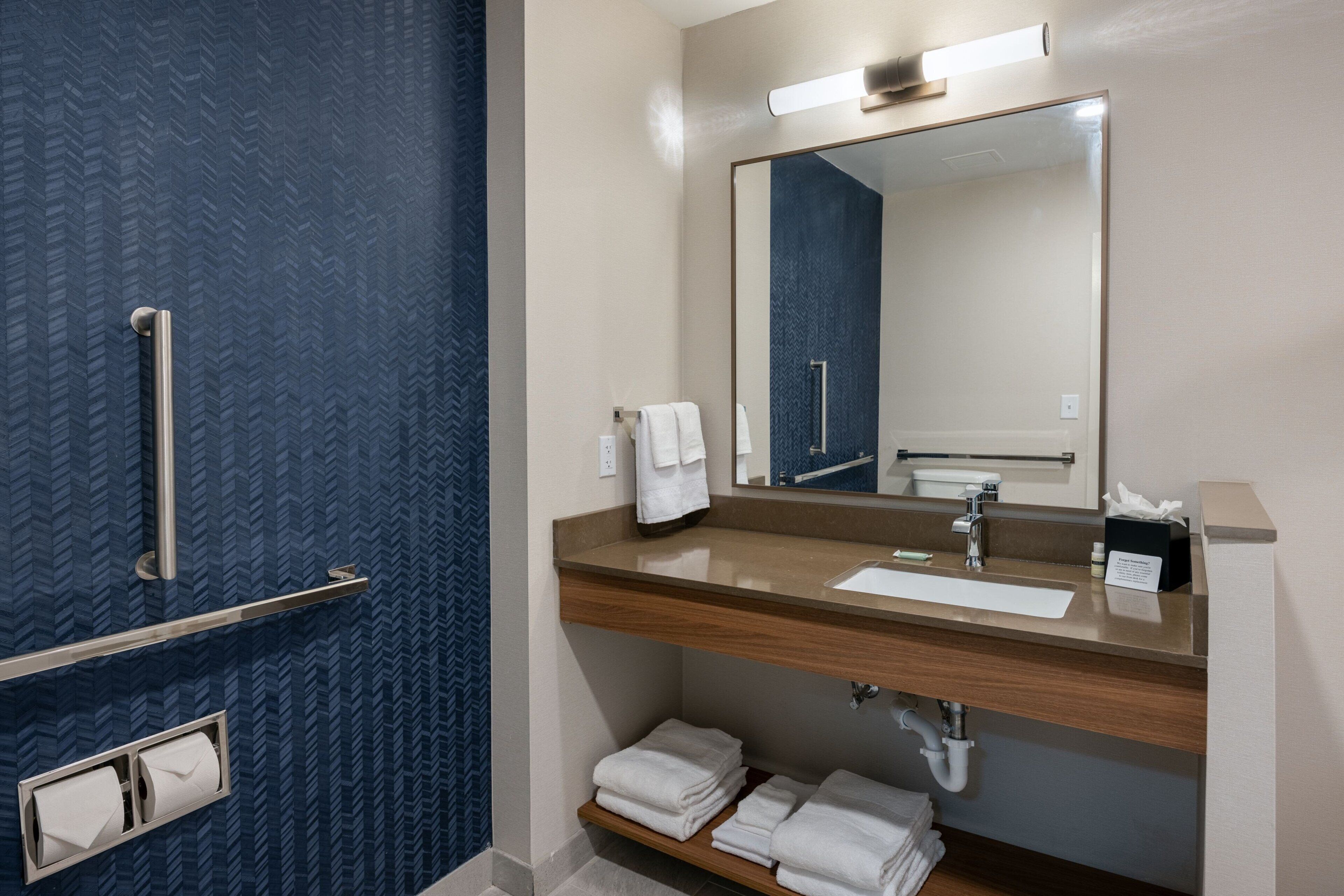 Une salle de bain avec un mur bleu à texture, un meuble-lavabo en bois avec un miroir, un porte-serviettes et une étagère avec des serviettes pliées.
