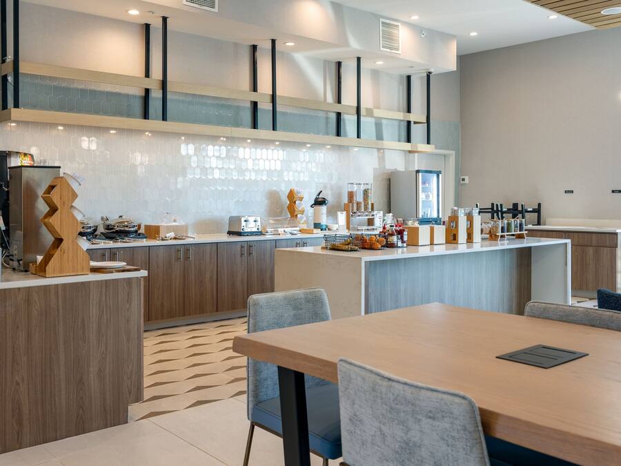 Una cocina moderna con una isla central, electrodomésticos integrados y un comedor con mesa y sillas de madera.