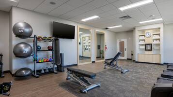 Une salle de sport équipée de matériel d’exercice, d’un banc et d’un mur recouvert de miroirs.