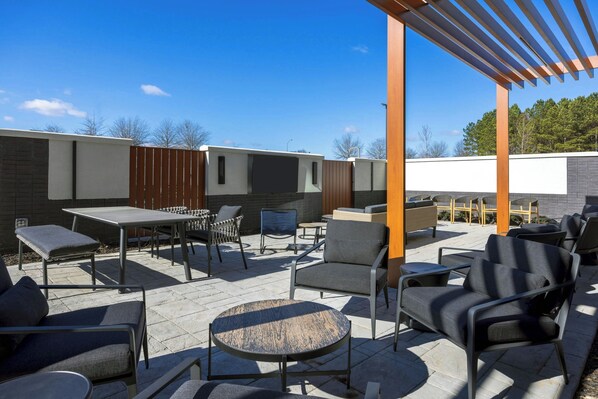 An outdoor patio area with a pergola, seating arrangements, and a brick wall.
