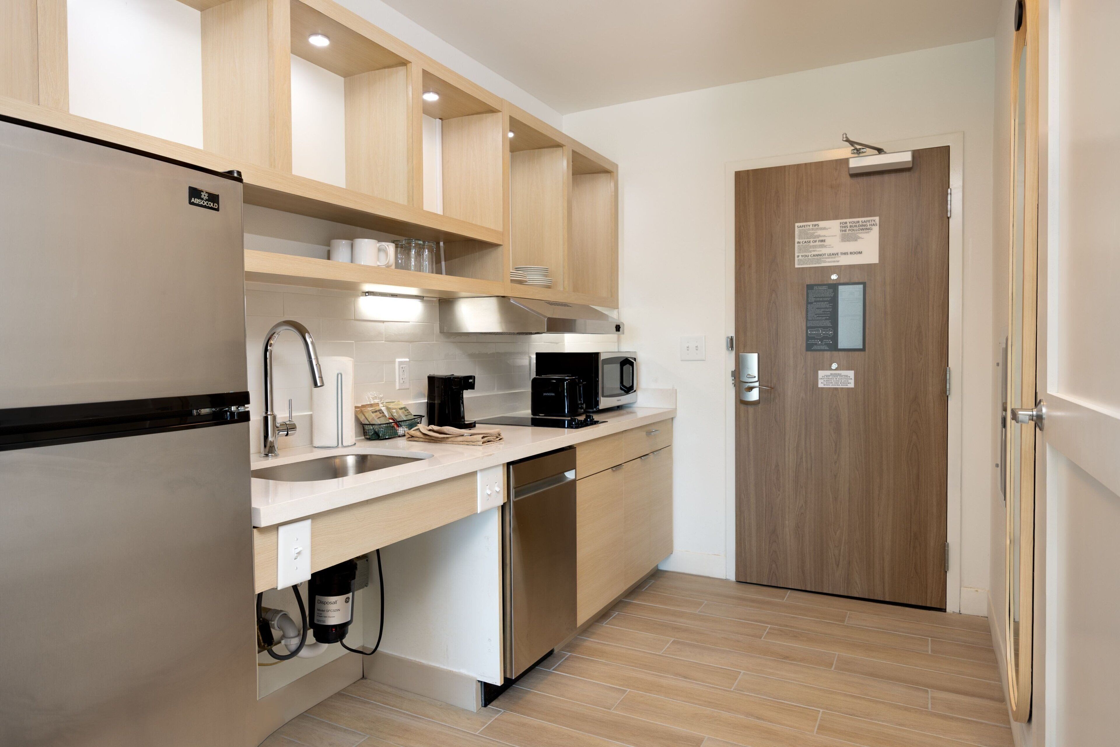 A modern kitchen with a stainless steel refrigerator, a coffee maker, and a microwave. There is a wooden door with a sign above it.