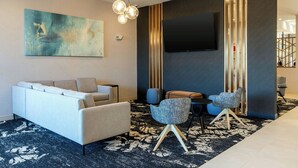 A modern living room with a sofa, two armchairs, a coffee table, and a flat-screen TV mounted on the wall.