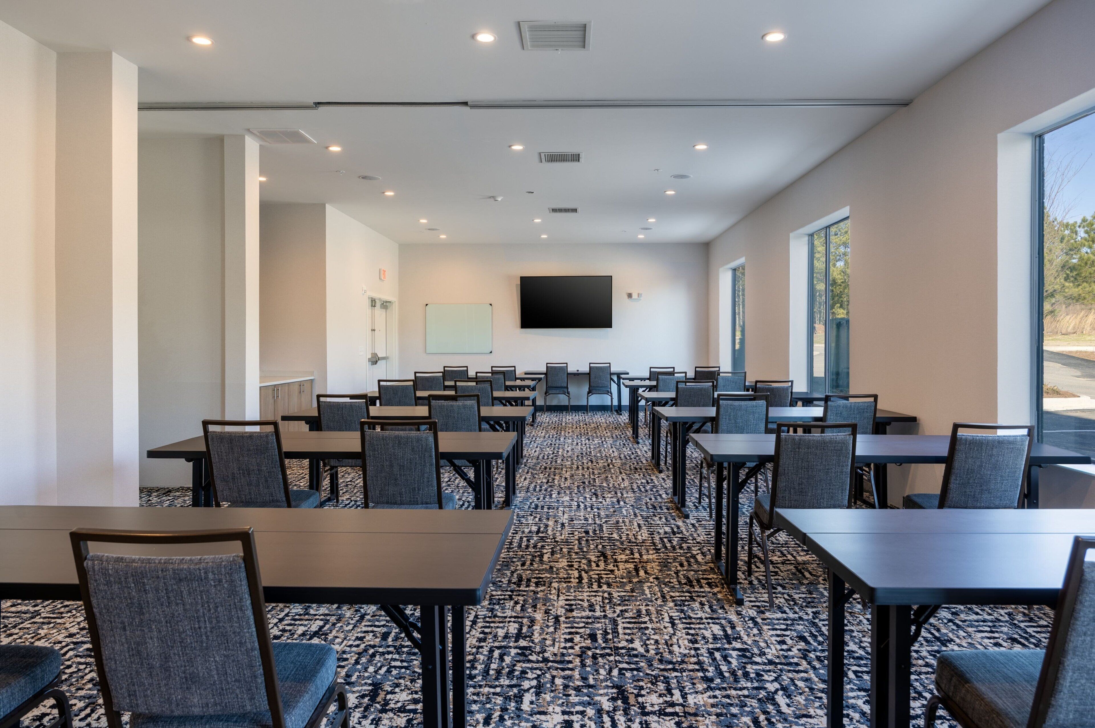 A conference room with tables and chairs, a large screen, and a carpeted floor.