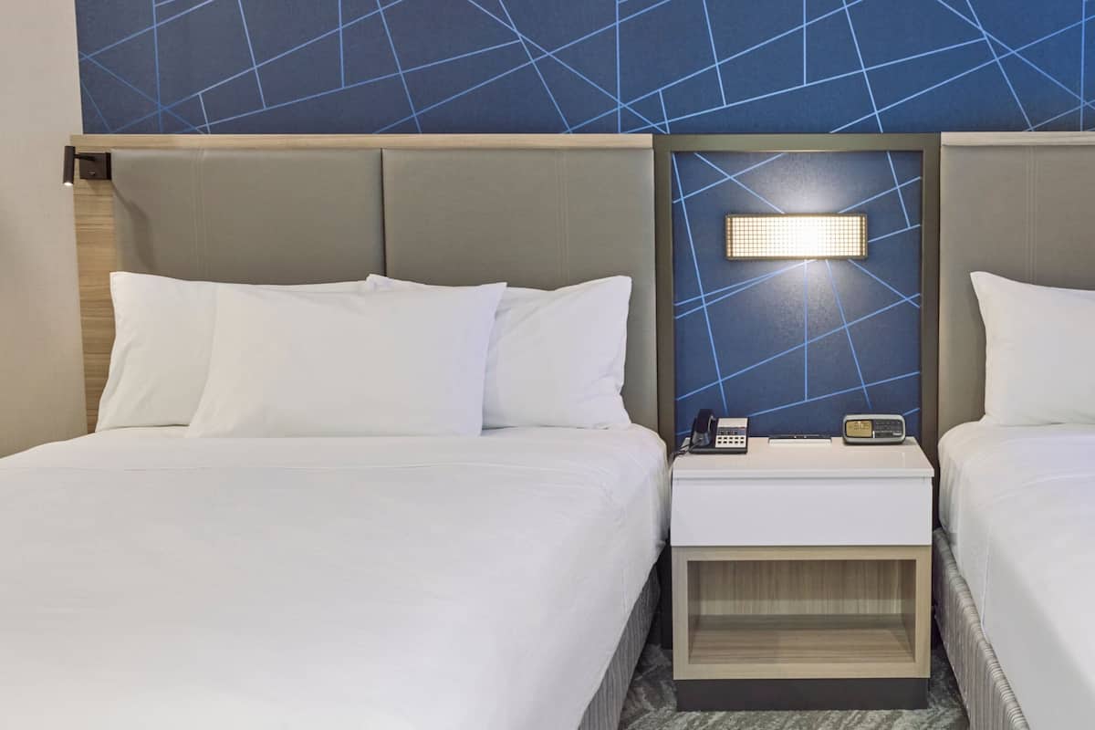 Une chambre d’hôtel avec deux lits, une table de chevet avec un téléphone et une lampe, et un mur orné d’un motif géométrique.