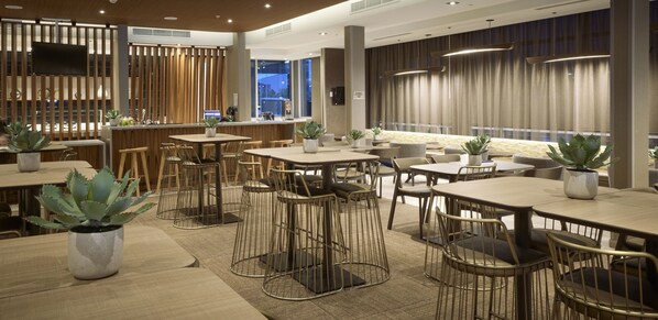 Un restaurante moderno con divisiones de madera, varias mesas y sillas, y plantas en macetas.
