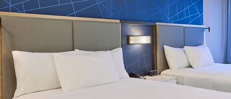 A hotel room with two beds, a nightstand, a wall-mounted lamp, and a geometric-patterned wall.