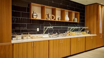 Una cocina moderna con armarios de madera, salpicadero de azulejos negros y una vitrina de vidrio con alimentos.