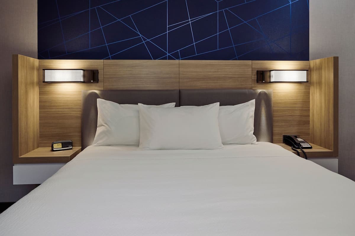 Une chambre d’hôtel avec un grand lit, deux tables de chevet, une petite table et un luminaire fixé au mur.