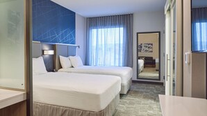 Une chambre d’hôtel avec deux lits, une grande fenêtre avec des rideaux légers, un miroir et une vue sur une autre chambre.
