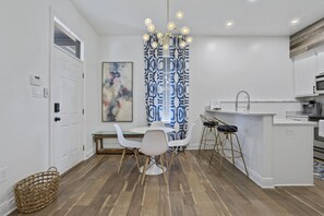 A modern kitchen with white cabinets, a wooden floor, a dining area with white chairs, and a unique blue and white patterned curtain. - BSL Dream Baycation - 2 blocks to Old Town! (Bay St. Louis)