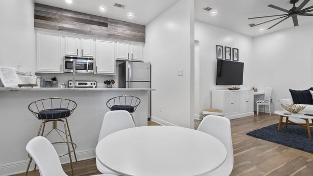 Une cuisine moderne avec des meubles blancs, des appareils en acier inoxydable et un coin repas comprenant des chaises blanches et une table ronde.