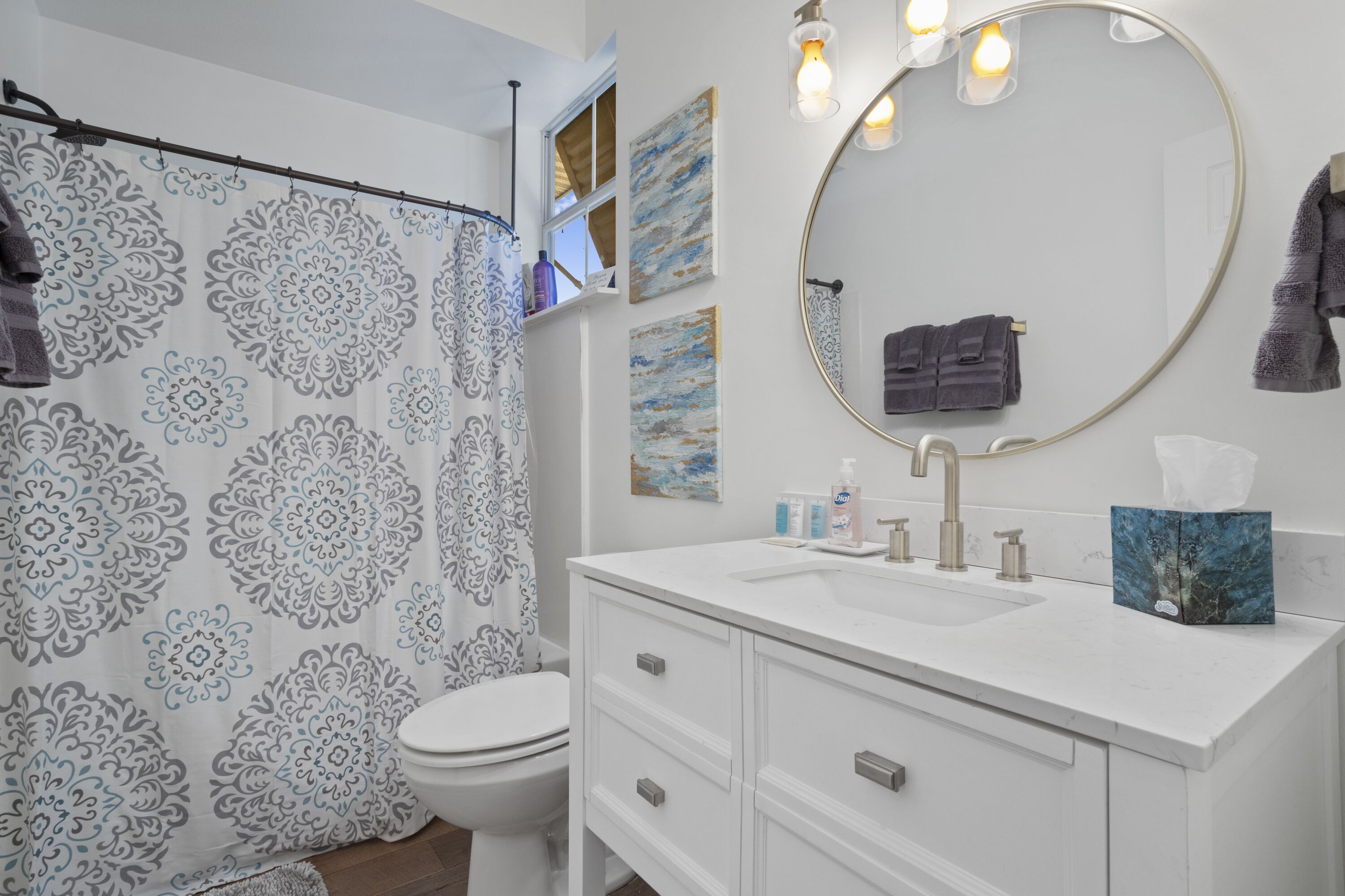 A bathroom with a shower curtain, toilet, sink, and a mirror.