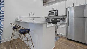 Une cuisine moderne avec des meubles blancs, des appareils en acier inoxydable et un îlot central doté de tabourets.