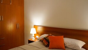 A hotel room with a wooden wardrobe, a bedside table with a lamp, and a bed with white and orange pillows. - Histórico: 1-bedroom apartment in San Blas market area. Independent living room! (Cusco)