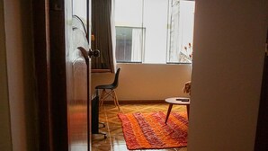 A hallway leading to a room with a tiled floor, a chair, a small round table, and a patterned rug. - Histórico: 1-bedroom apartment in San Blas market area. Independent living room! (Cusco)