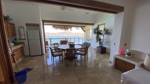 A spacious living area with a dining table and chairs, a kitchen with cabinets and a refrigerator, and a balcony with a view of the sea. - Luxurious Pacifica Grand Senior Suite (Zihuatanejo)