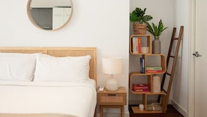 Ein Schlafzimmer mit einem Bett, einem Nachttisch mit Lampe, einem Spiegel, einem Bücherregal und einer Tür.