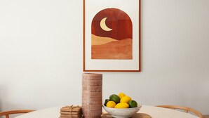 Ein Esstisch mit einem gerahmten Kunstwerk, einer hohen Vase und einer Schüssel mit Zitronen und Limetten.