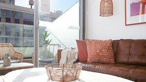 Ein modernes Wohnzimmer mit einem braunen Ledersofa, Korbstühlen, einem Glastisch und einem großen Fenster mit Blick auf die Stadt.