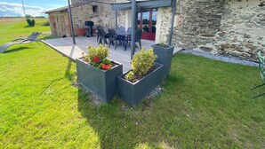 Een stenen gebouw met een overdekt terras, zitplaatsen buiten en bloembakken met bloemen.