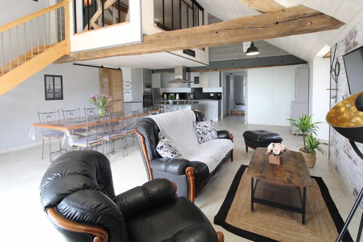 Un vaste espace de vie doté d’un haut plafond, une table à manger avec des chaises, un canapé, un fauteuil en cuir noir et une table basse.