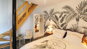 Een slaapkamer met een bed, een nachtkastje, een stoel, een houten trap en een muur met een palmboom muurschildering.